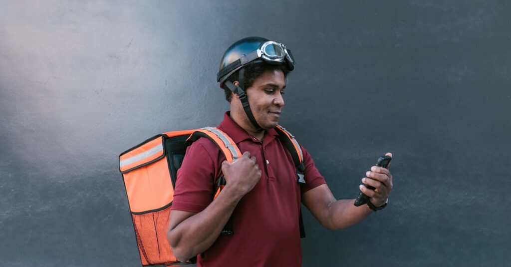 a delivery courier wearing a helmet and backpack checks his smartphone against a dark background