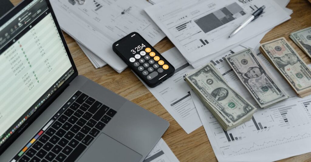 a desk with financial documents currency a laptop and phone calculator