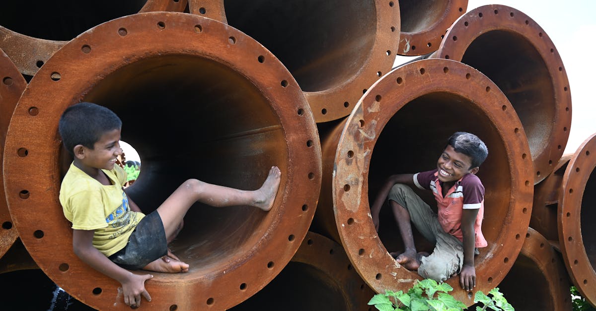 two boys enjoy playful moments inside large metal pipes smiling and interacting joyfully outdoors