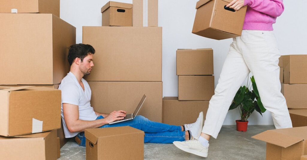 young couple settling in new apartment surrounded by packing boxes managing tasks on a laptop