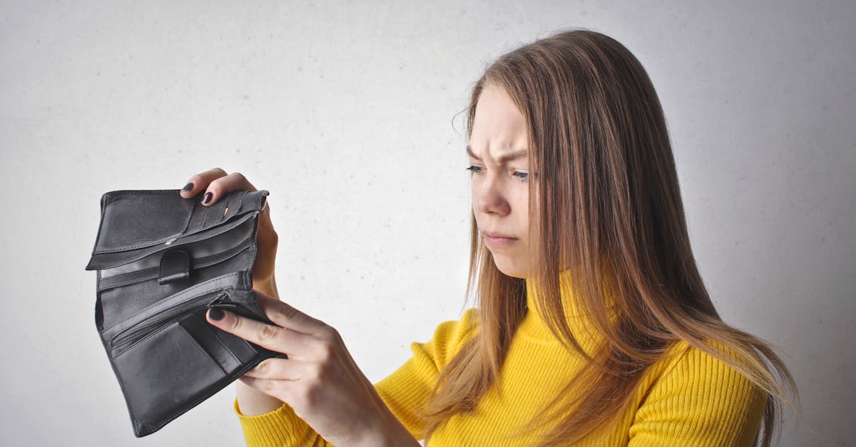 young woman in a yellow top looking at her empty wallet with a frustrated